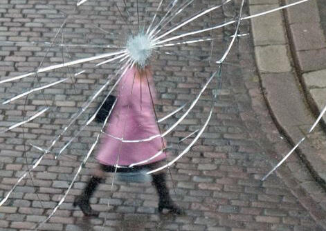 woman in pink coat walking as pictured through window with crack in the glass that covers woman's face